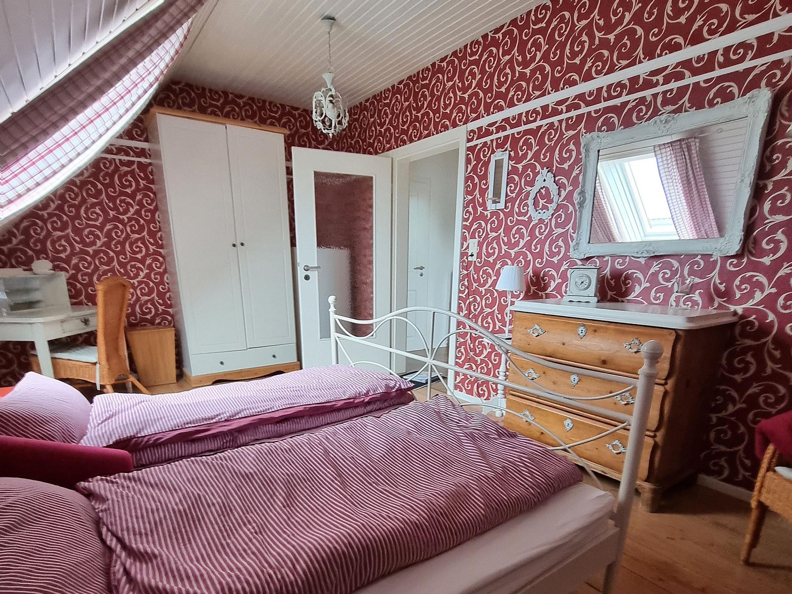 Bedroom with bed, wardrobe, and dressing table. Red-and-white wallpaper. Skylight with roller shutter.