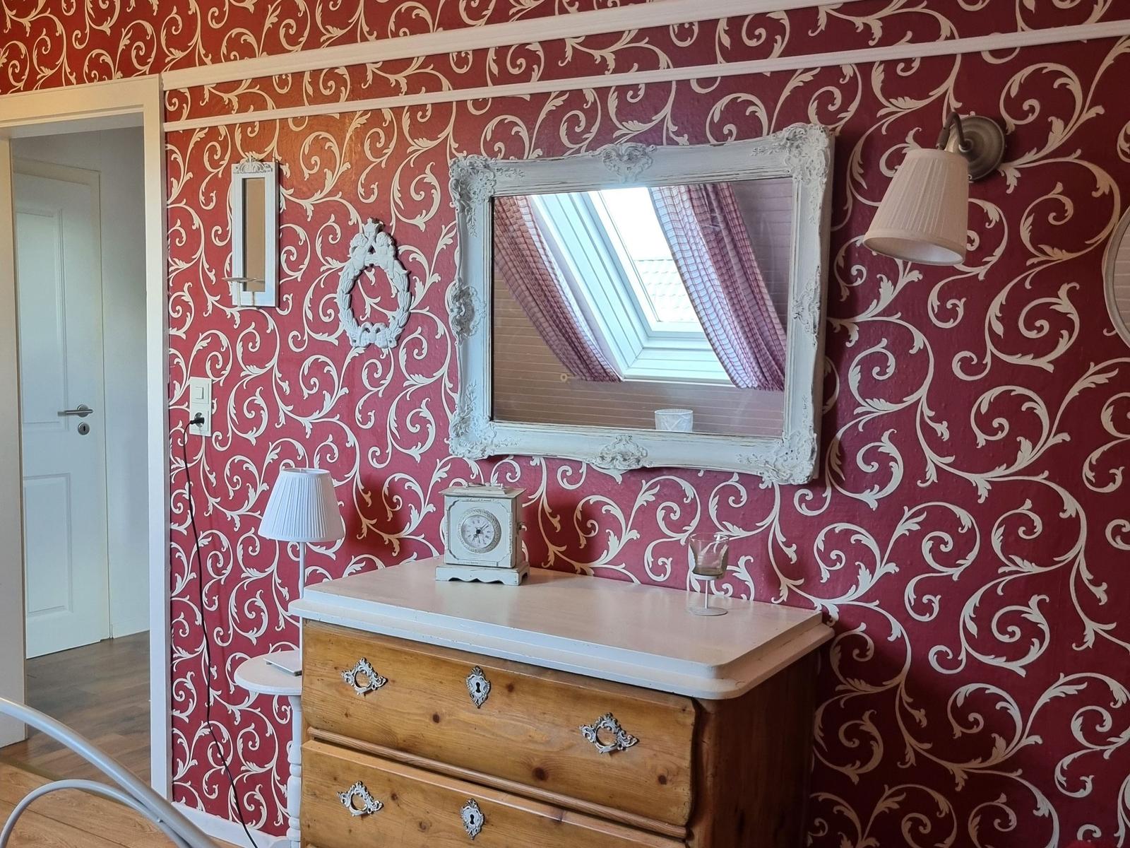 Bedroom with patterned red walls, mirror, and wooden dresser.