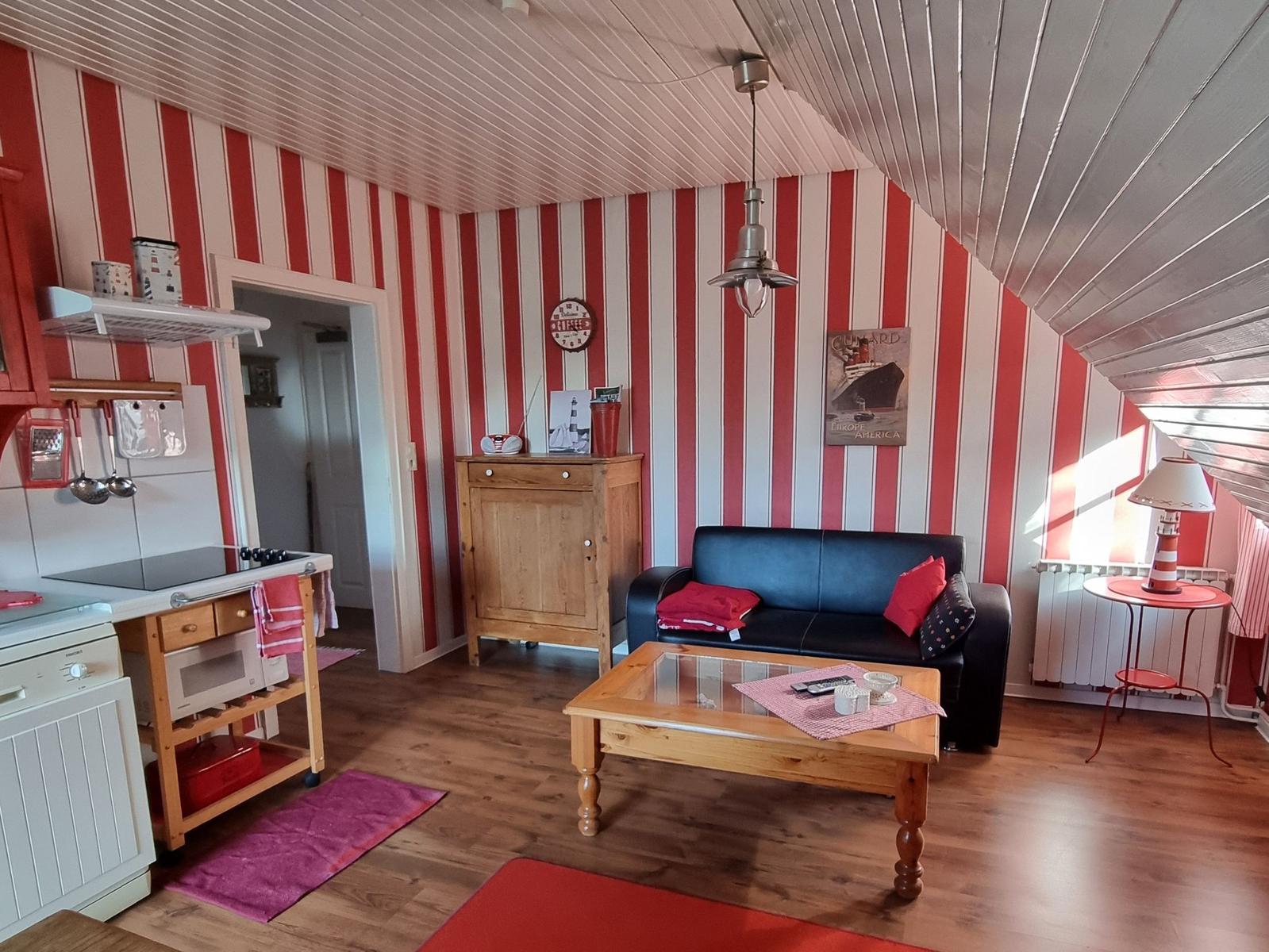 Living and kitchen area with red stripes, sofa, and wooden table.