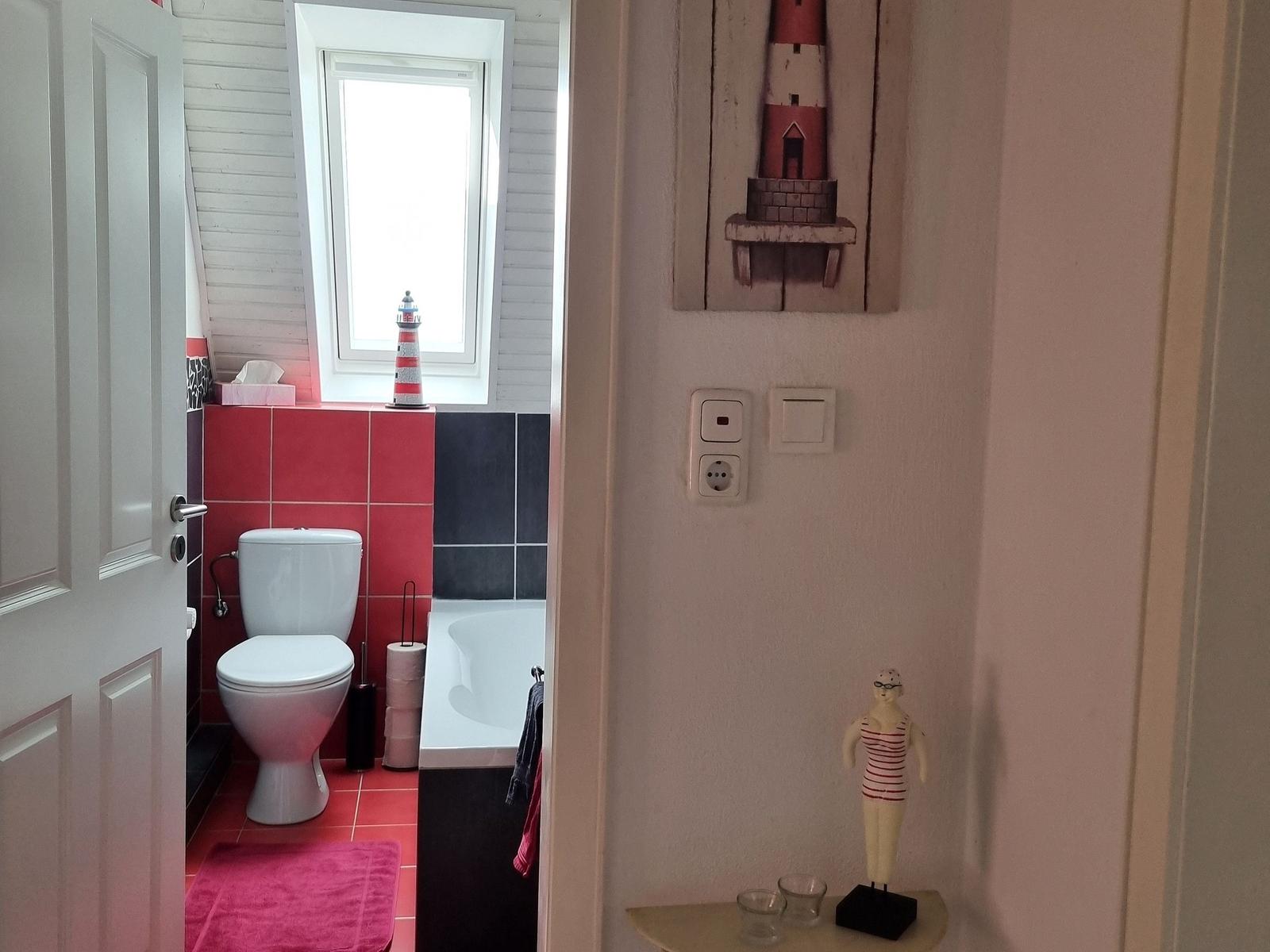 Bathroom with toilet, bathtub, and window. Hallway decorated with wall art and swimmer figurine.