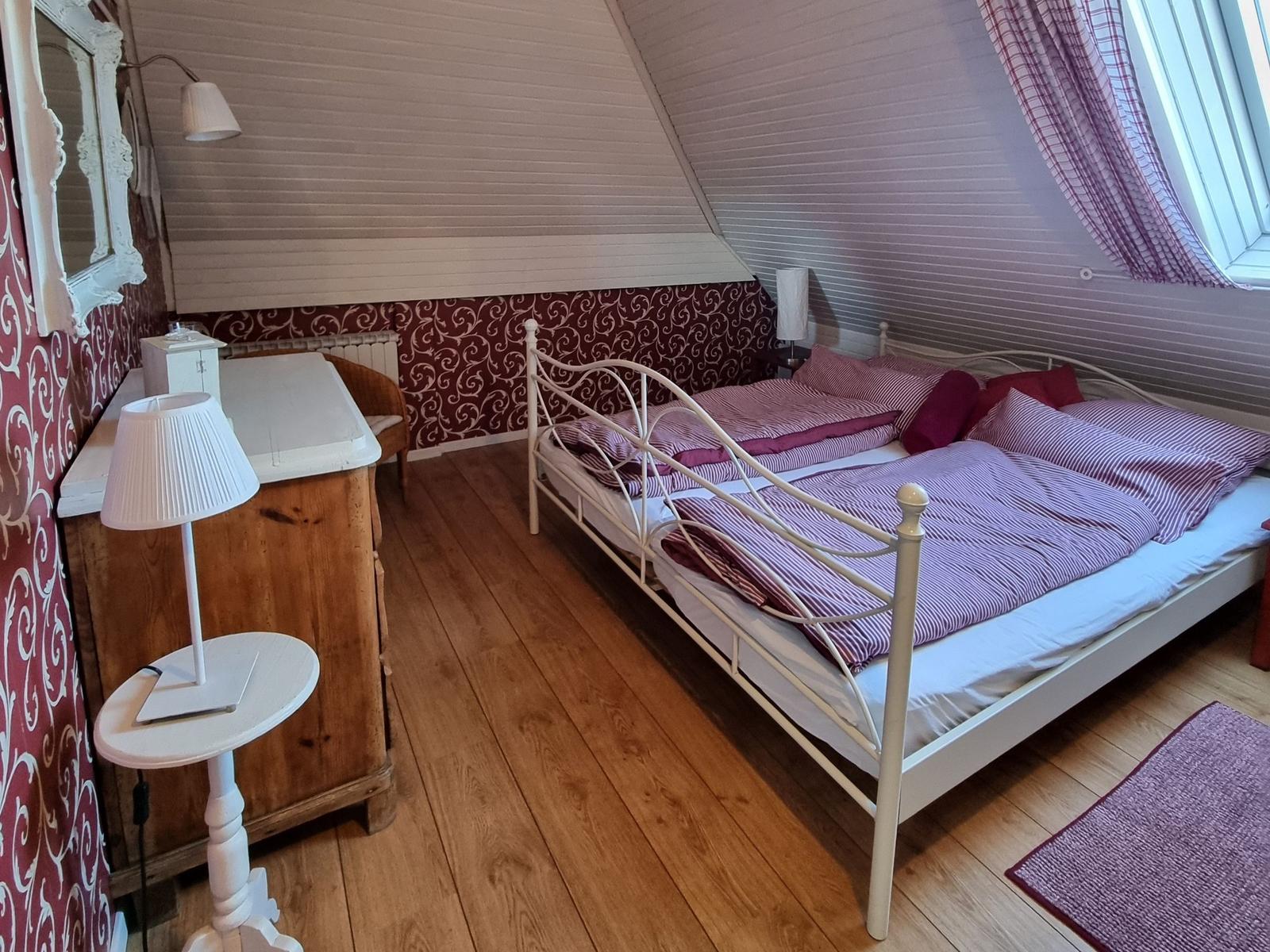 Double bed with striped bedding, wooden floor, and window with curtains.