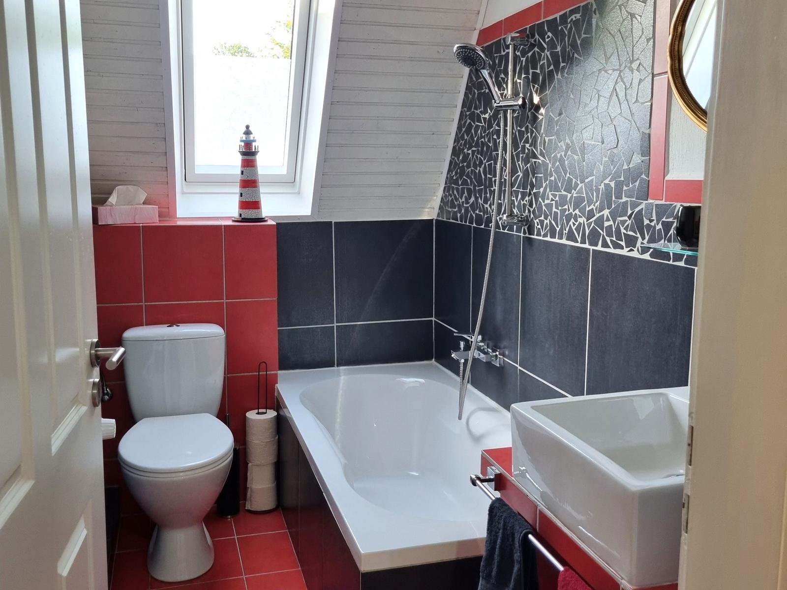 Bathroom with bathtub, sink, and toilet. Walls tiled in red and black.