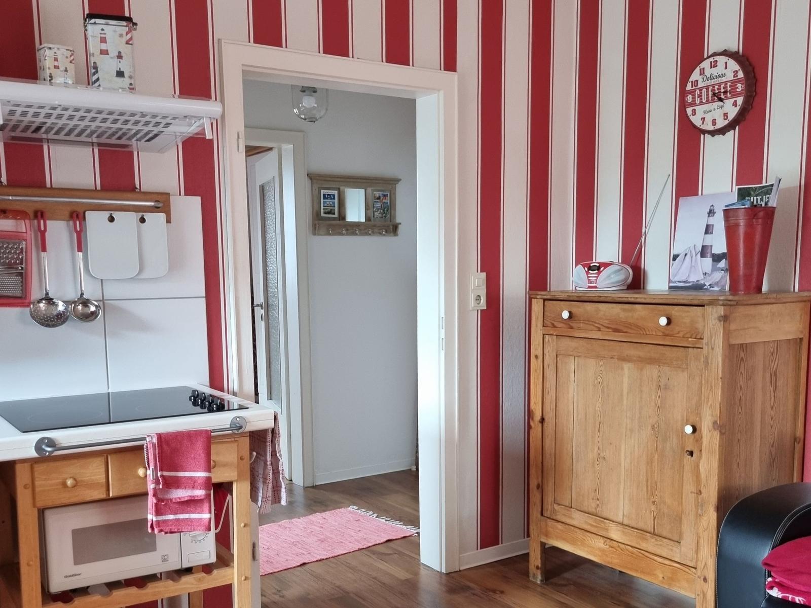 Kitchen with wooden furniture and red striped walls. Passage to a hallway with wooden floor.