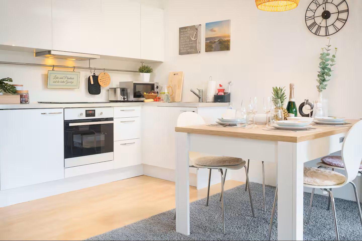 Küche mit Essbereich, weißer Arbeitsfläche und Holztisch mit Stühlen.