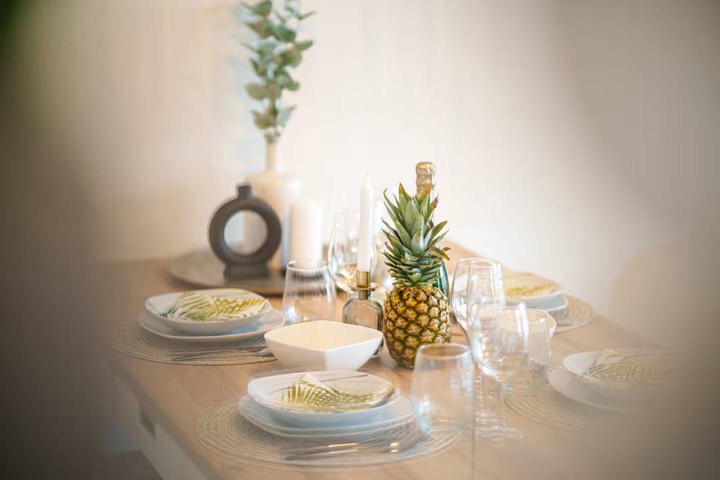 Tisch gedeckt mit Teller, Gläsern und einer Ananas als Zentrum.