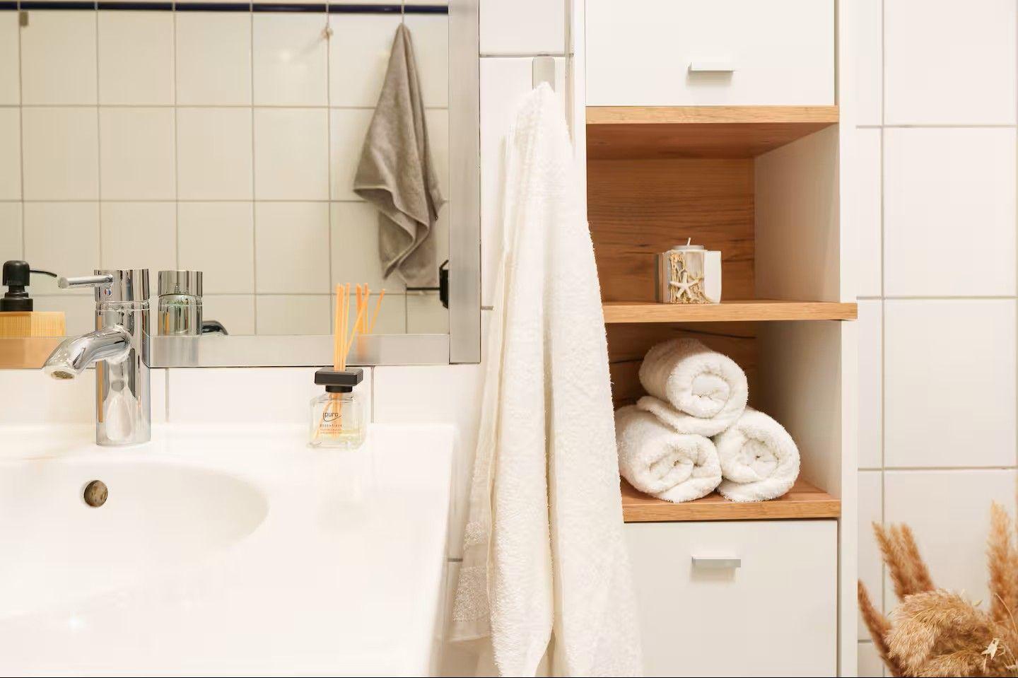 Bad mit Waschbecken, Spiegel, Handtuch und Handtüchern auf Holzregal.