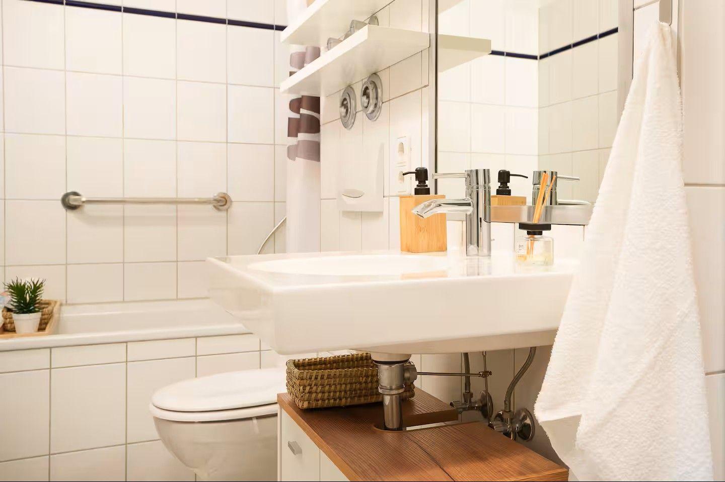 Badezimmer mit Waschbecken, Toilette und Dusche. Weiße Fliesen, Spiegel und Handtuch.