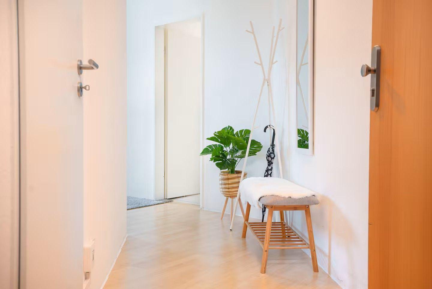 Flur mit Sitzbank, Pflanze und Kleiderständer. Holzboden und weiße Wände.
