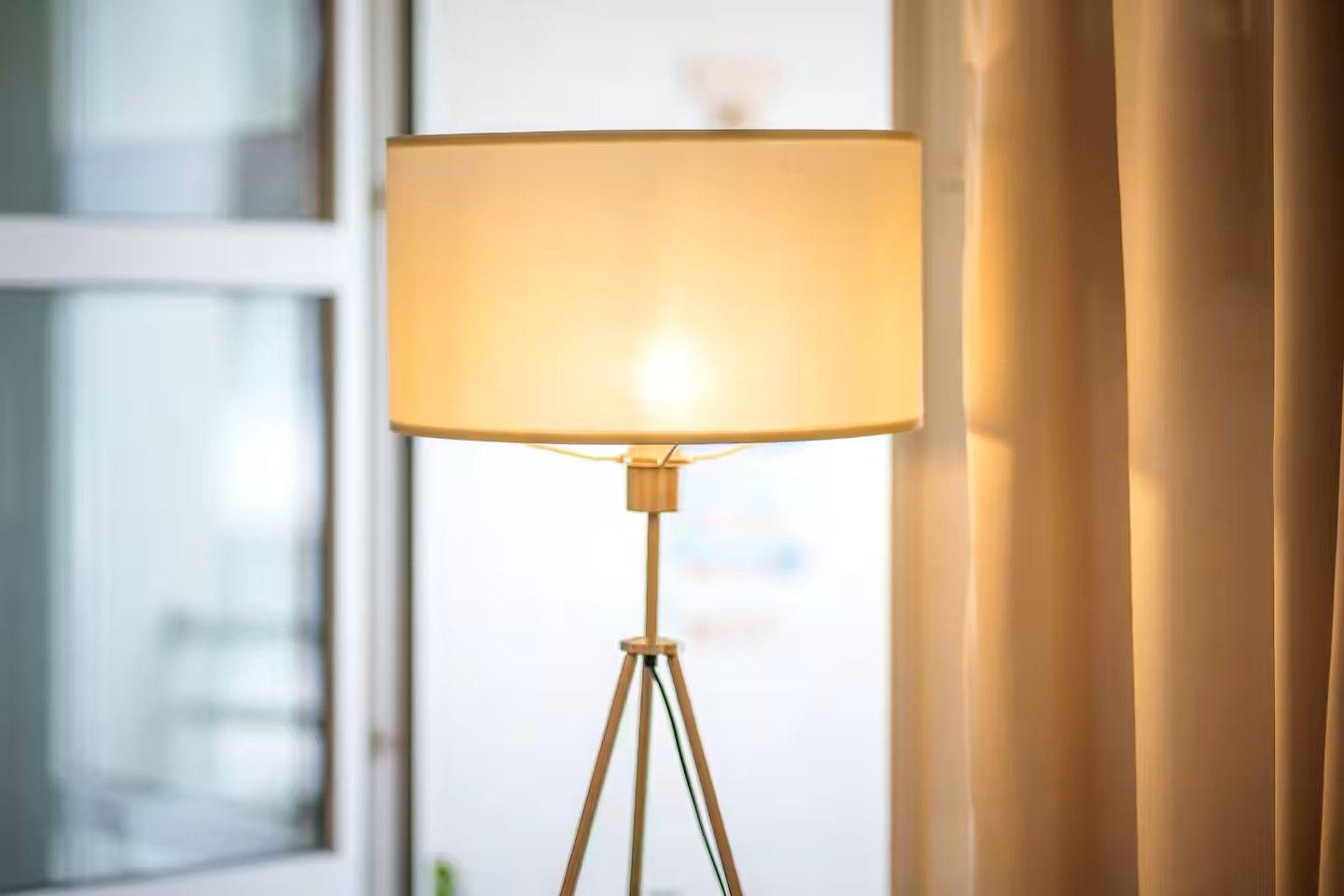 Eine Stehlampe mit einem hellen Schirm steht neben einem Fenster und Vorhängen.