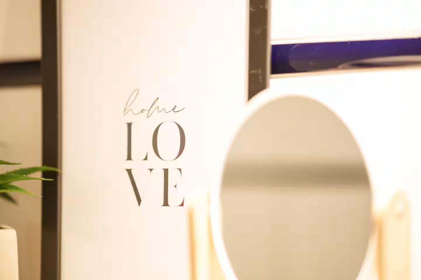 Wand mit Aufschrift home LOVE, runder Spiegel und Pflanze