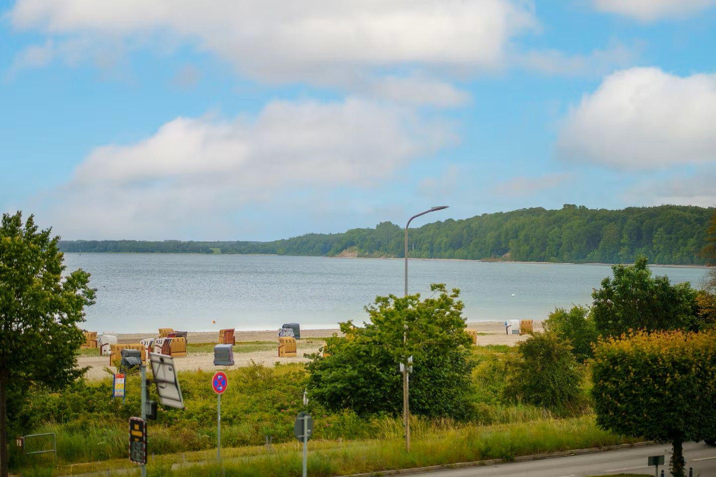 Strand mit Strandkörben und Wald im Hintergrund unter blauem Himmel mit Wolken.