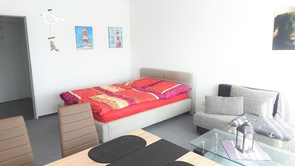 Schlafzimmer mit Bett, Sofa und Esstisch. Wandbild mit Leuchtturm.