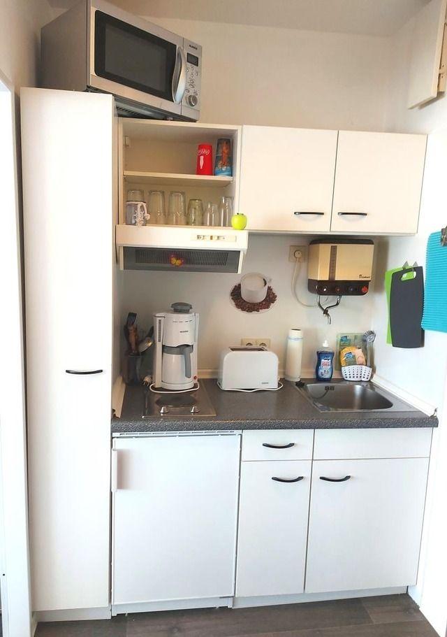 Küche mit weißen Schränken, Spüle, Kaffeemaschine und Mikrowelle.