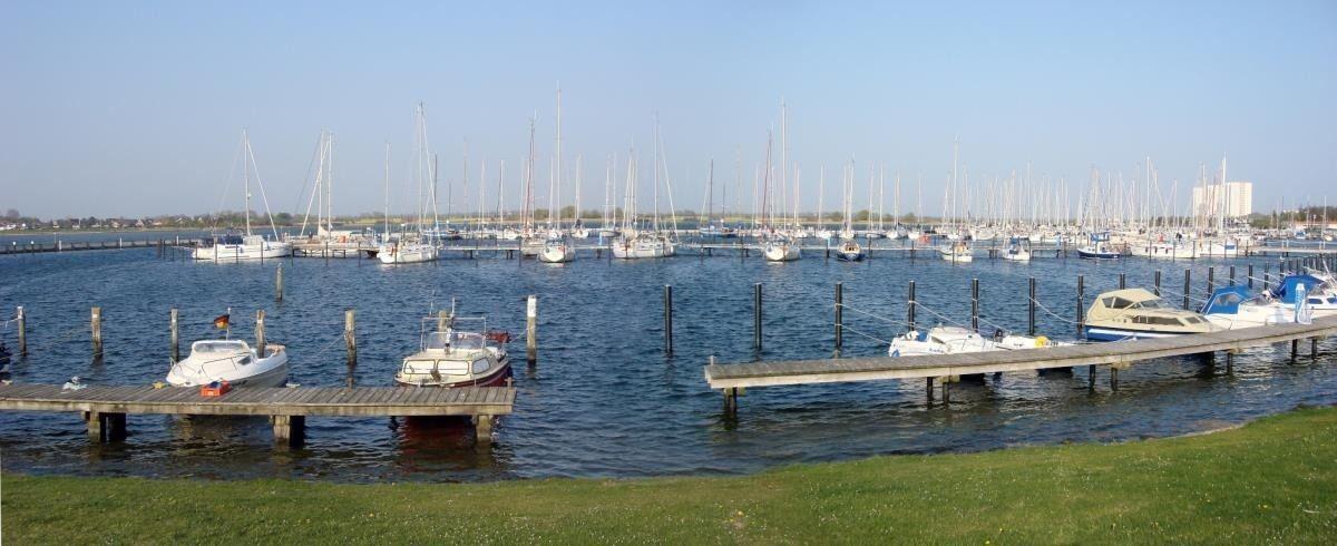 Hafen mit Booten und Stegen, Blick auf Wasser und Segelyachten im Hintergrund.