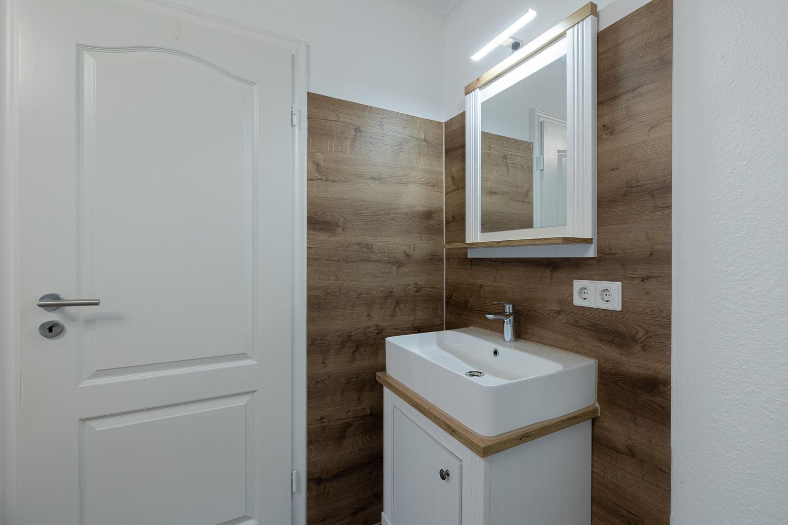 Badezimmer mit Waschbecken, Spiegel und Holzwand