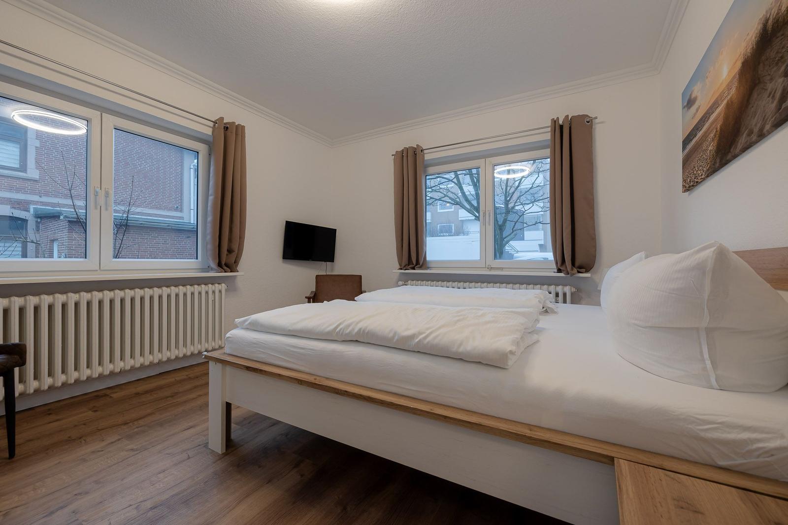 Schlafzimmer mit Doppelbett, zwei Fenstern und Wandbild.