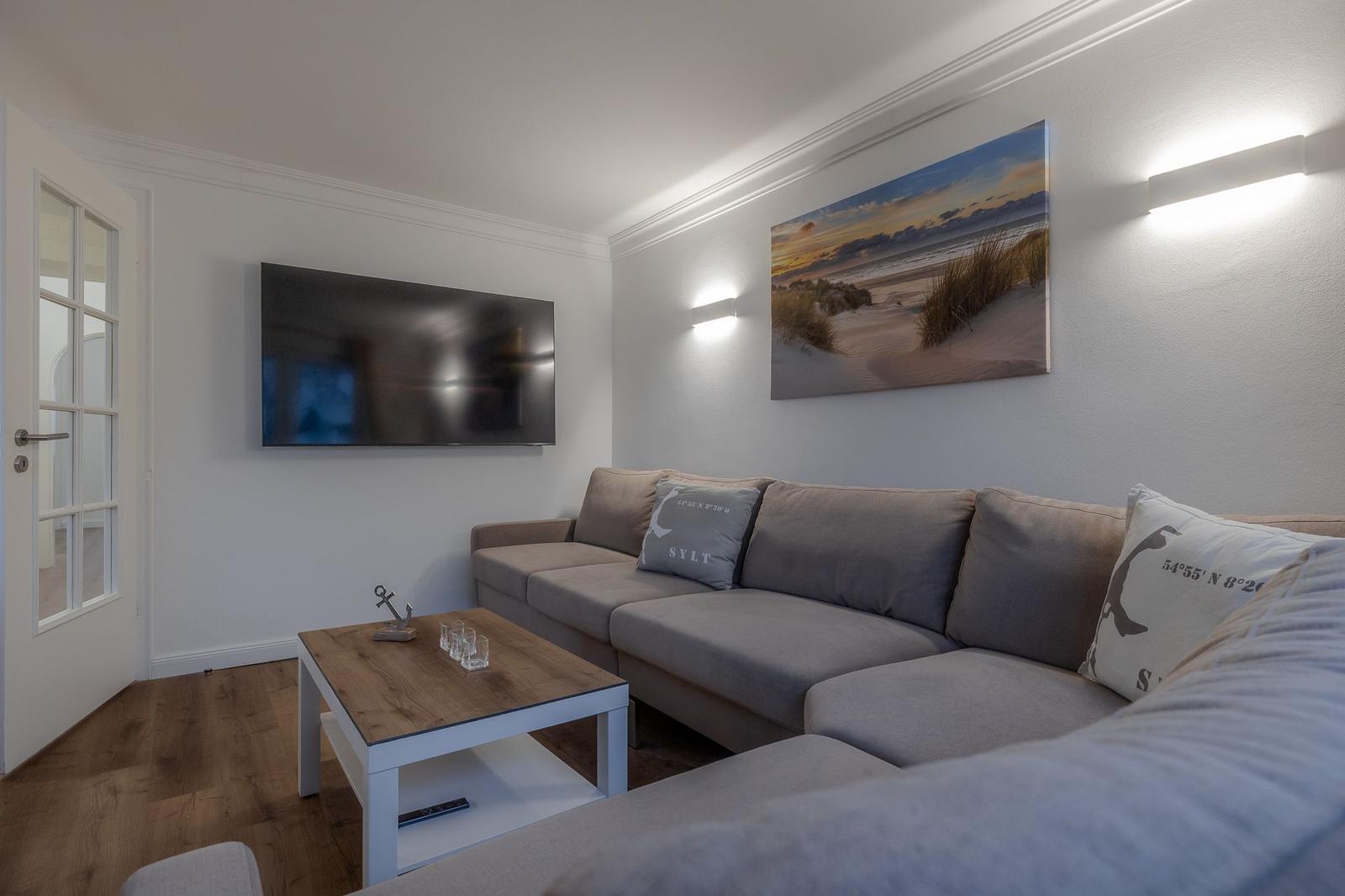 Wohnzimmer mit Sofa, Fernseher und Wandbild. Holzfußboden und Tür sichtbar.