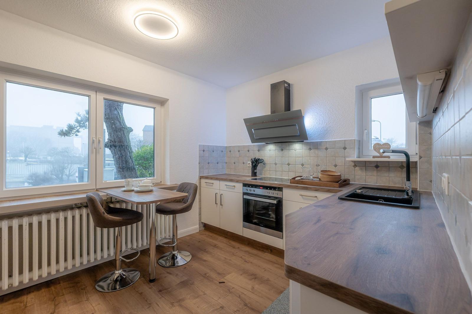 Küche mit Essbereich, Fenster, Kochfeld, Dunstabzug und Spüle.