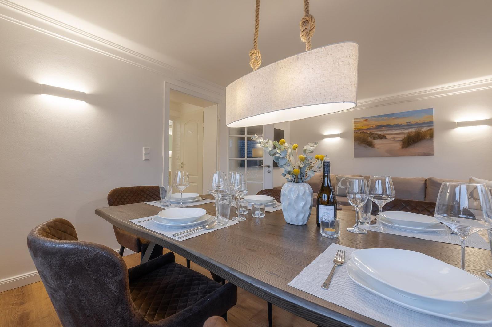 Esstisch mit Stühlen, Kerzen und Wein. Hängelampe und Wandbild im Hintergrund.
