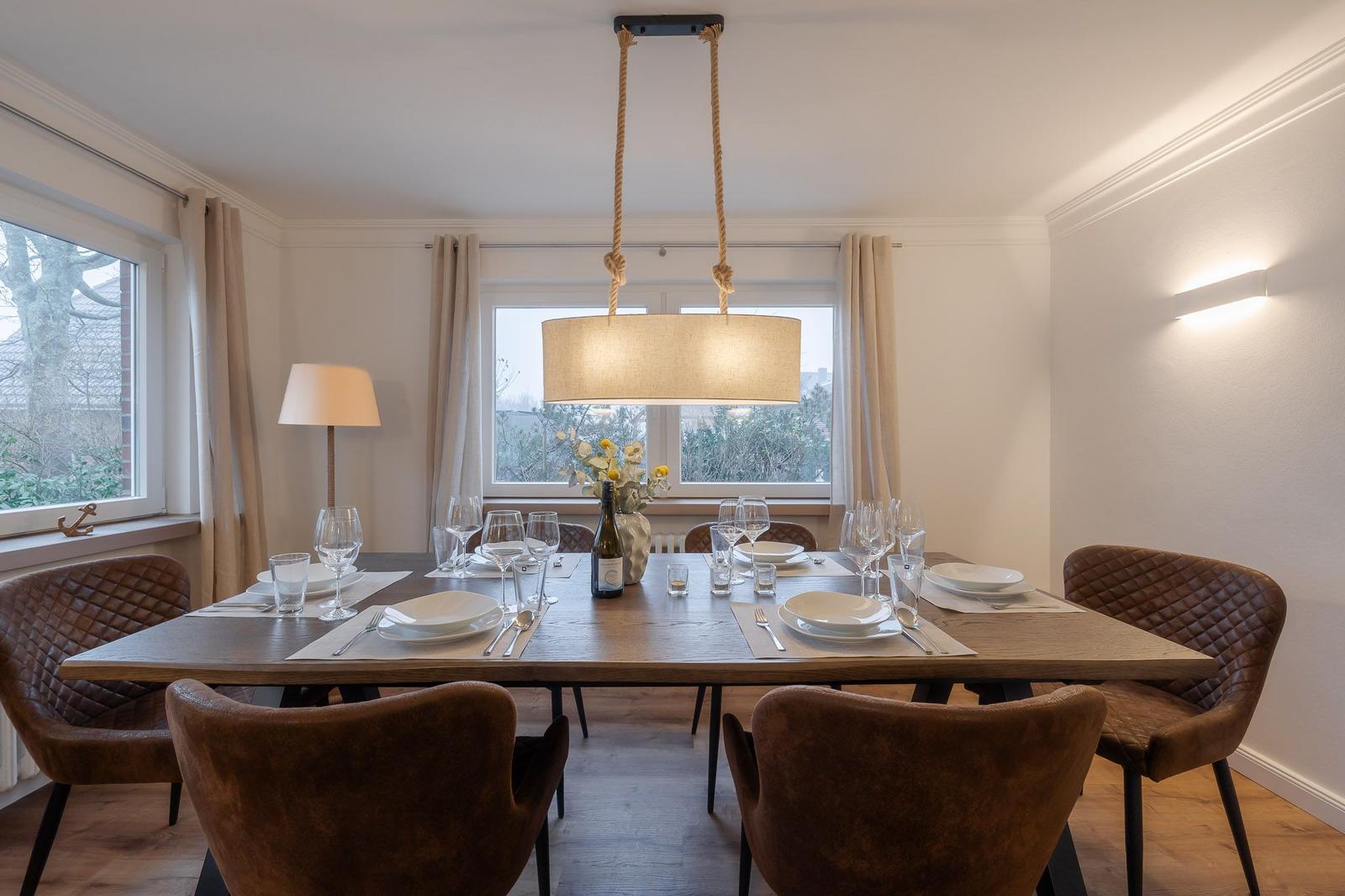 Esszimmer mit Holztisch, braunen Stühlen und Fenstern mit Blick nach draußen.