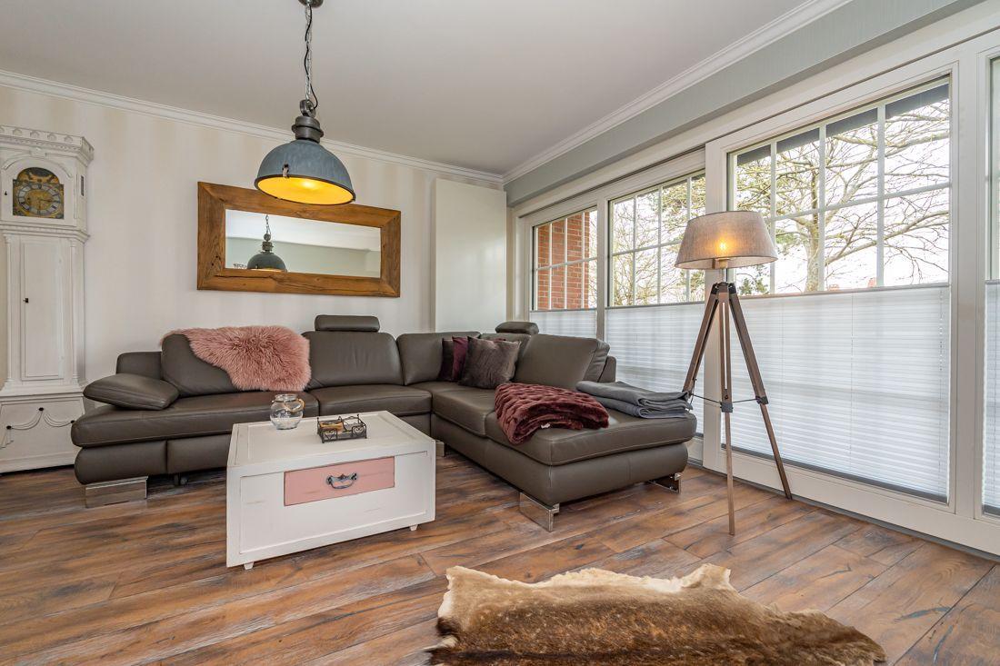 Wohnzimmer mit braunem Sofa, Holzboden und großen Fenstern.