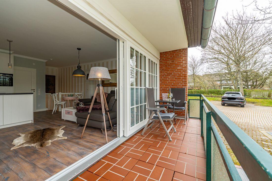 Terrasse mit Tisch und Stühlen, Blick ins Wohnzimmer mit Sofa und Küche.