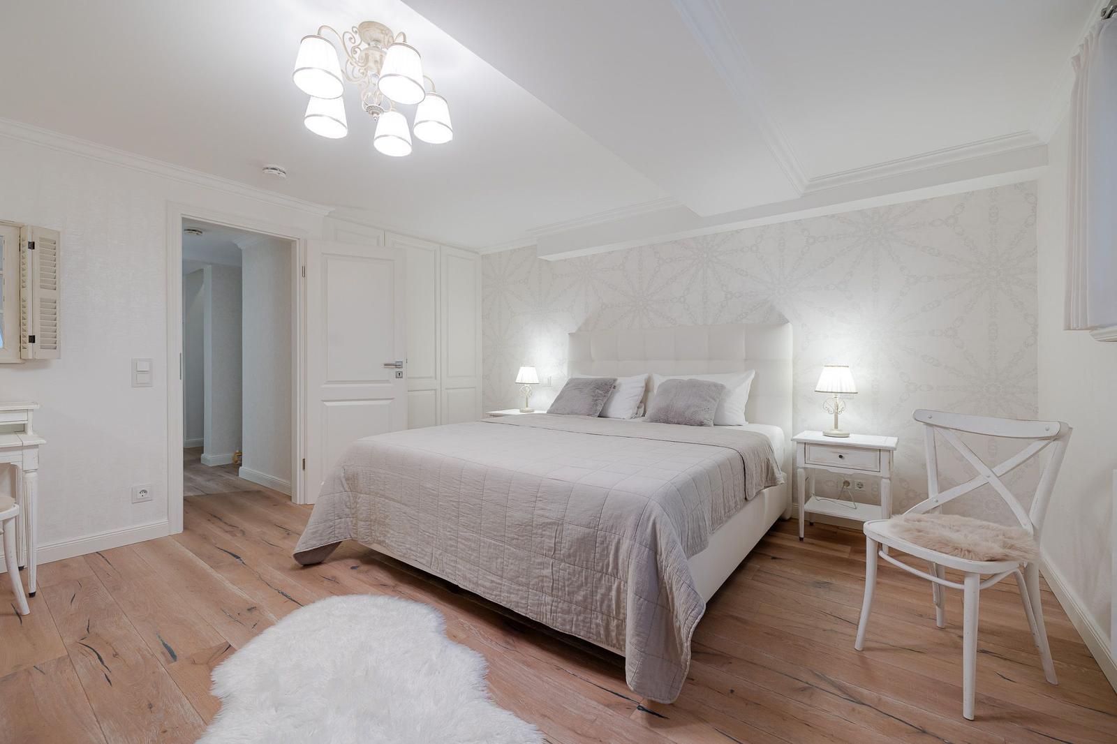 Schlafzimmer mit weißem Bett, Holzboden und Nachttischen mit Lampen.