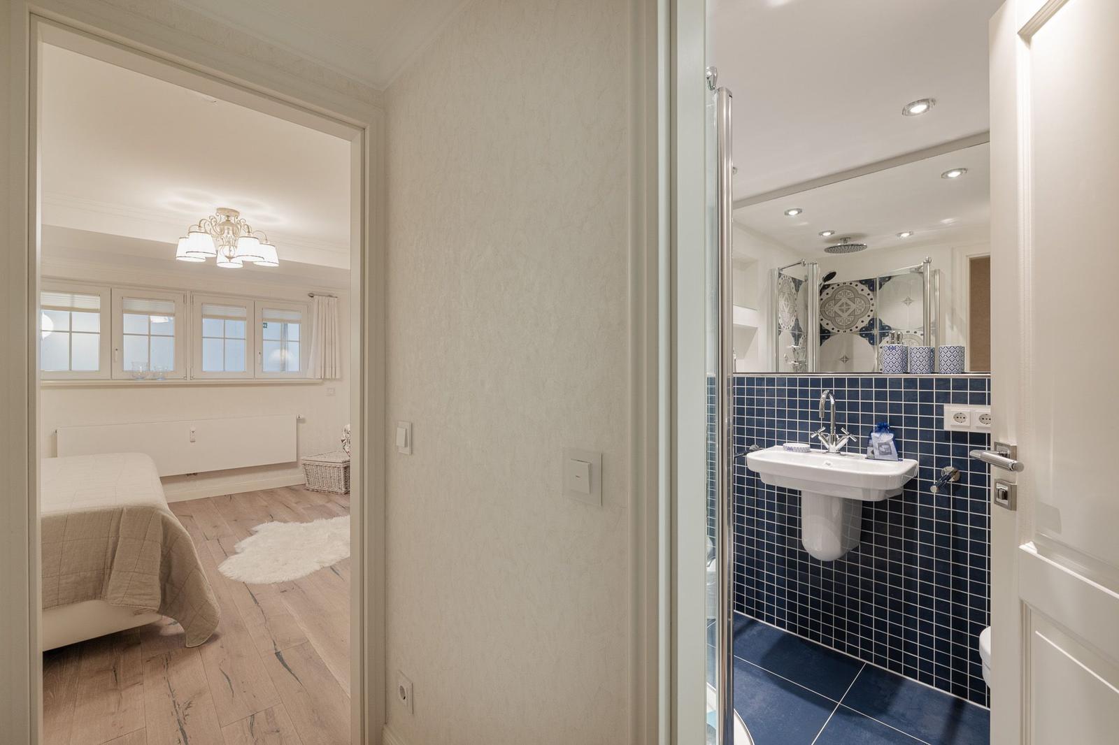 Schlafzimmer mit Bett und Fenster. Nebenraum mit Dusche und Waschbecken.