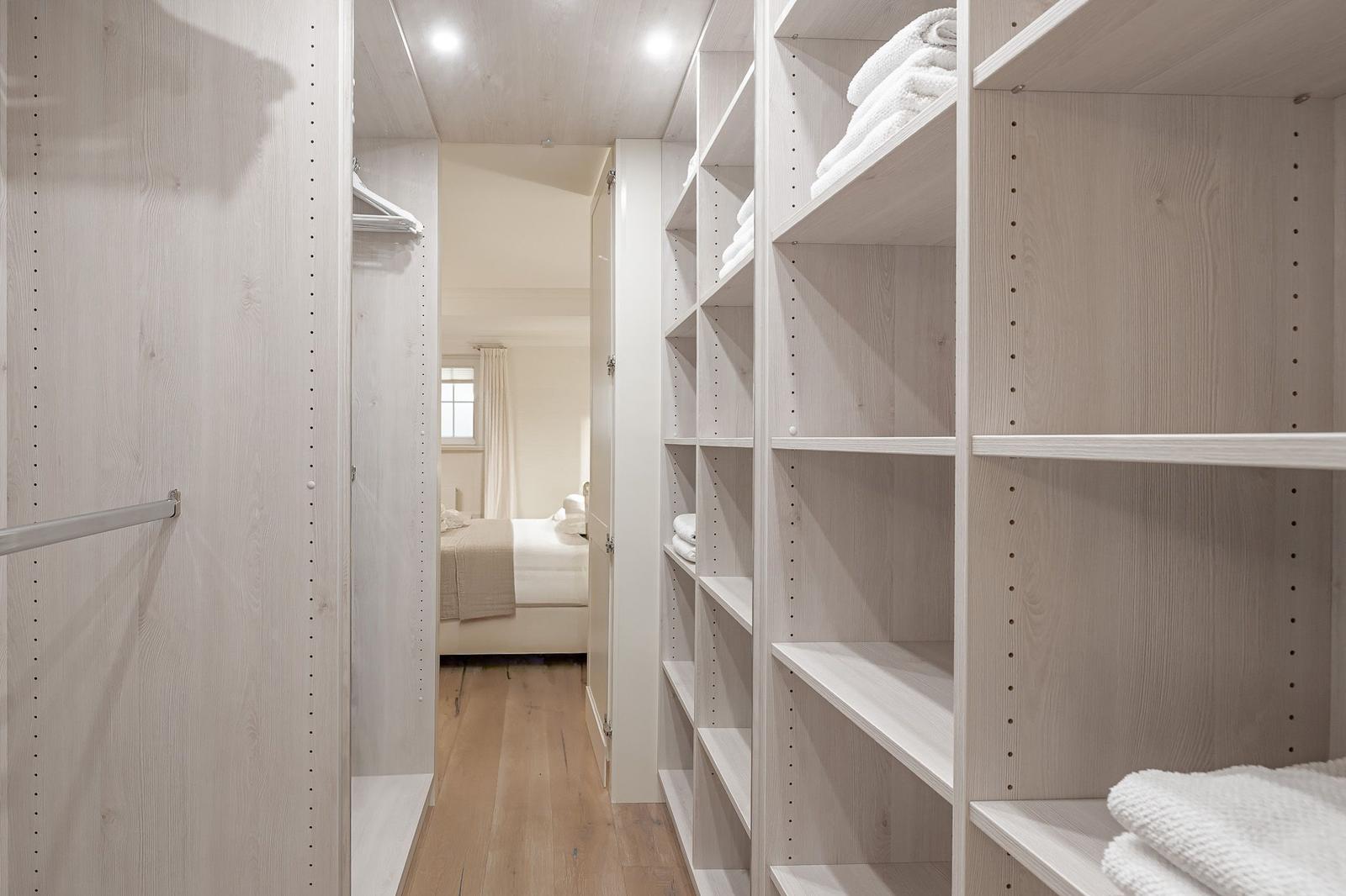 Großer Kleiderschrank mit Regalen und Kleiderstange. Im Hintergrund ist das Schlafzimmer zu sehen.