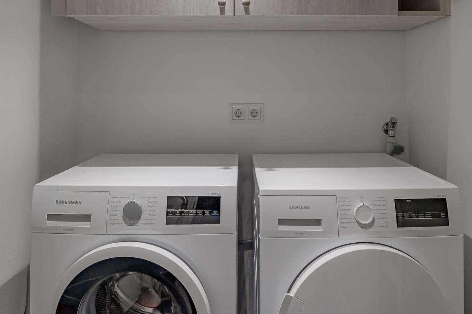 Waschmaschine und Trockner in einem Raum mit Schrank und Steckdosen.