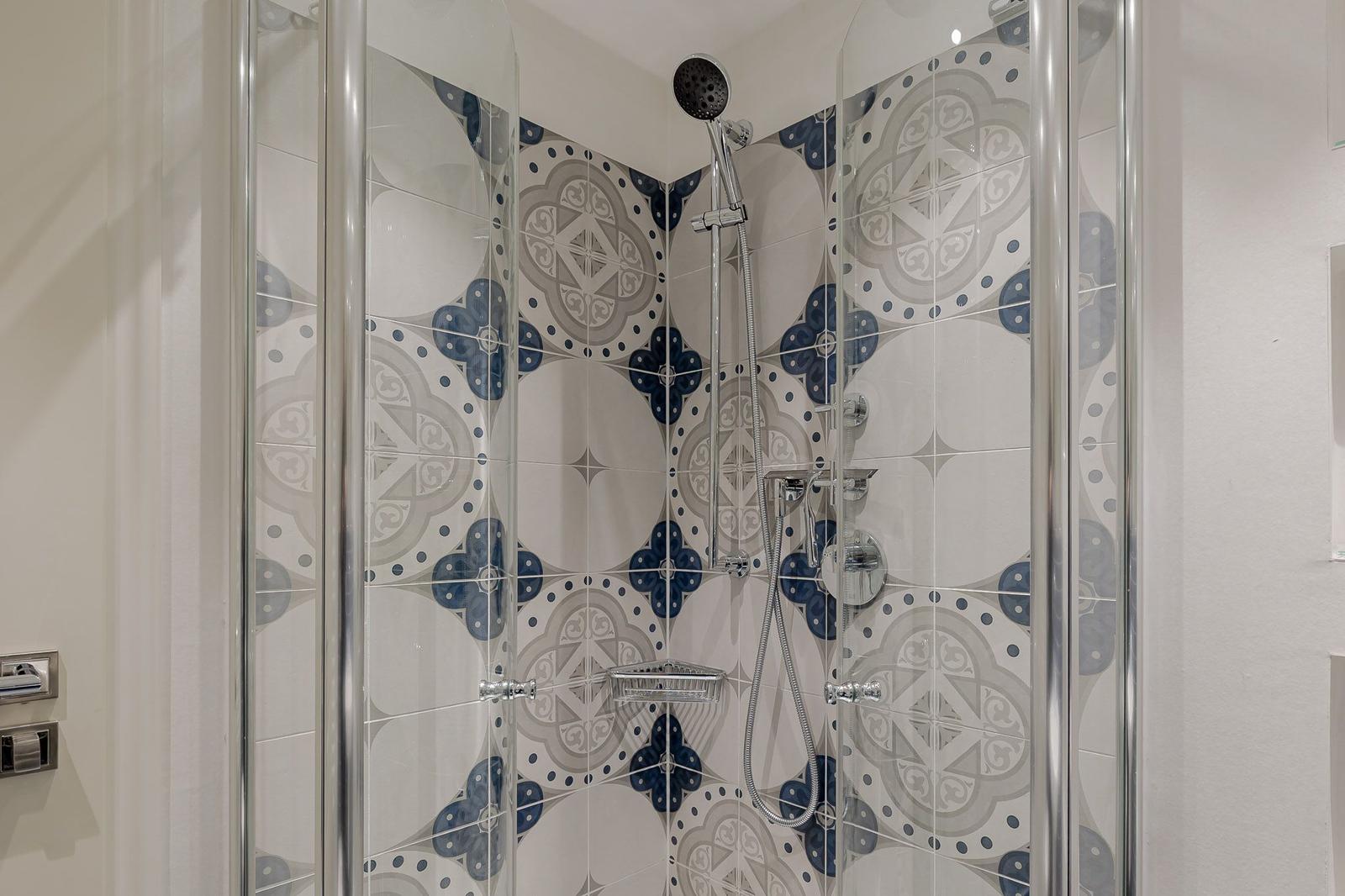 Duschkabine mit blau-weißen Mosaikfliesen und chromfarbenem Duschsystem.