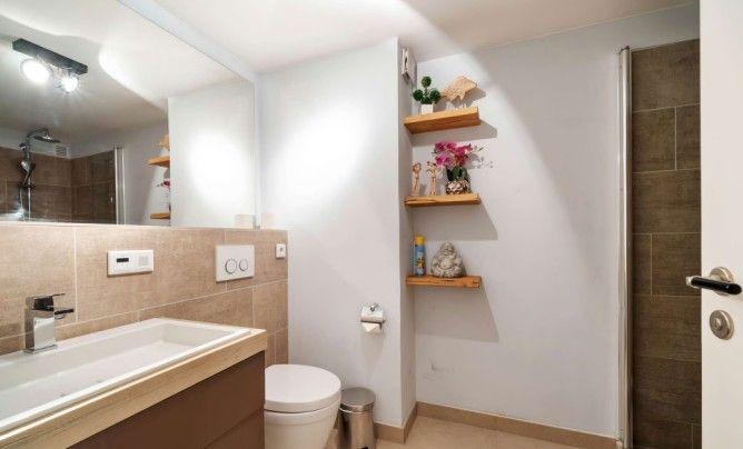 Badezimmer mit Waschbecken, Toilette und Dusche. Holzregale an der Wand mit Dekoration.