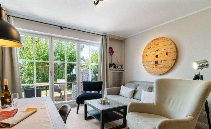 Wohnzimmer mit Sofa, Sessel und Tisch. Große Fensterfront mit Blick auf Garten.