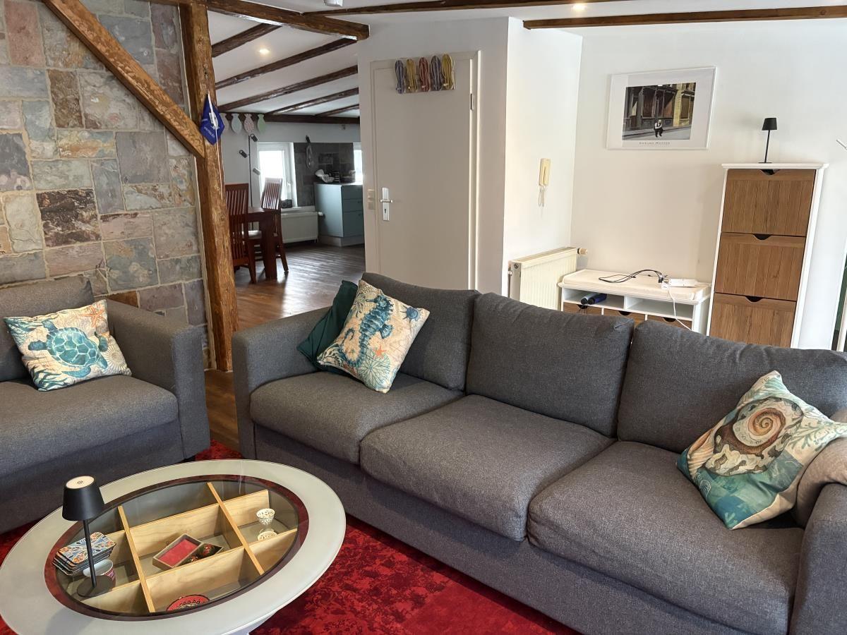 Wohnzimmer mit grauem Sofa, runden Tisch und Steinwand. Blick in die Küche.