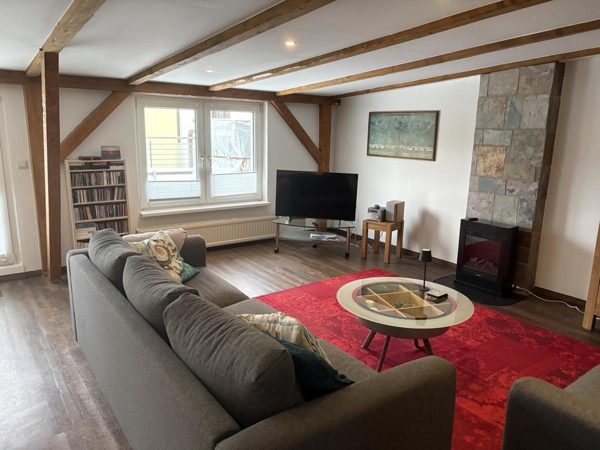 Wohnzimmer mit Sofa, Fernseher und Kamin. Holzbalken und roter Teppich.