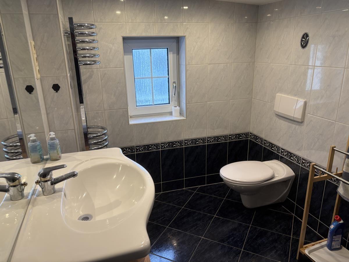 Badezimmer mit Waschbecken, Toilette und Fenster. Fliesen und Spiegel sichtbar.