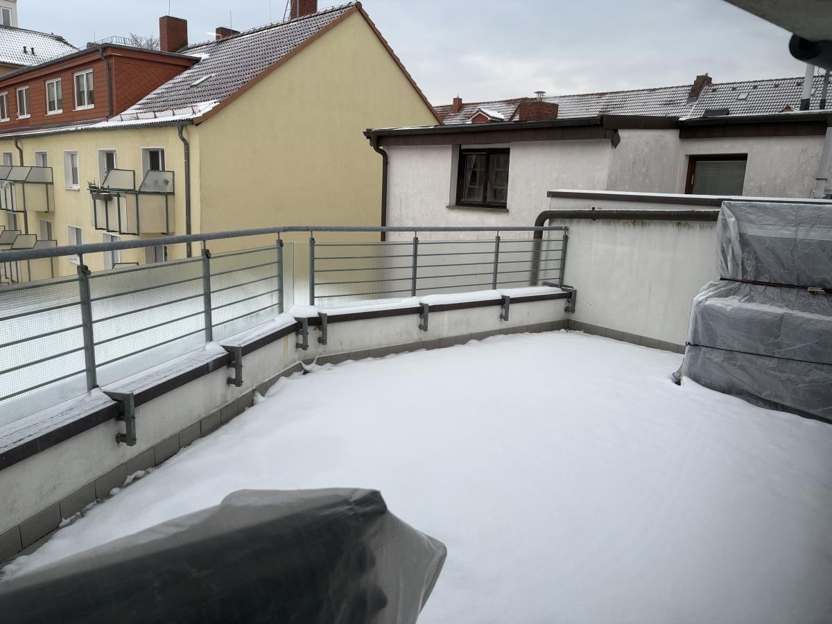 Schneebedeckter Balkon mit Metallgeländer und gedecktem Sitzmöbel.