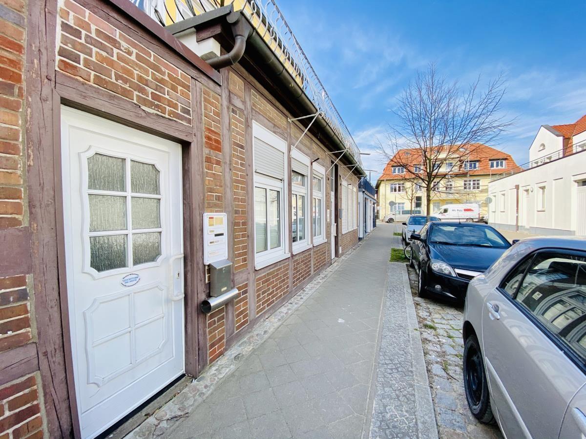 Haus mit weißen Fenstern und Tür, gepflasterte Straße mit geparkten Autos.