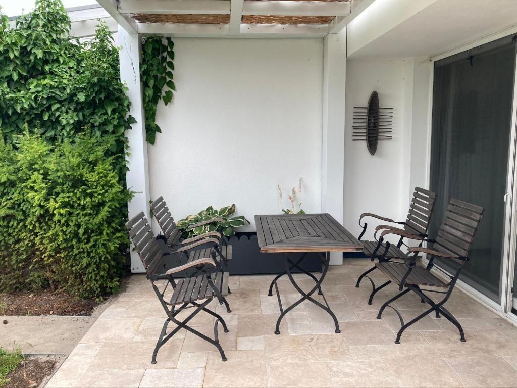 Terrasse mit Tisch und vier Stühlen, umgeben von Pflanzen und einer weißen Wand.