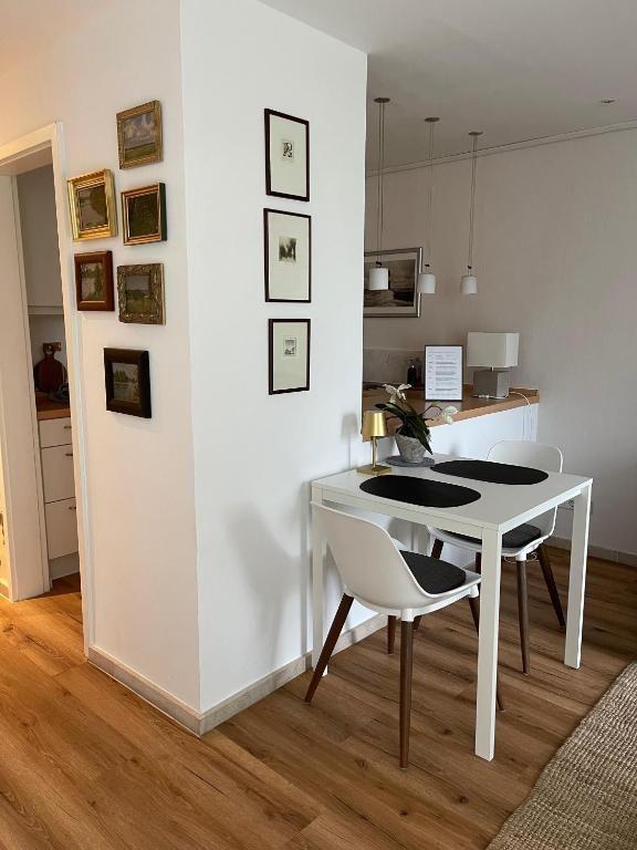 Essbereich mit Tisch und Stühlen, Wand mit Bildern, Holzboden und Küchenbereich im Hintergrund.