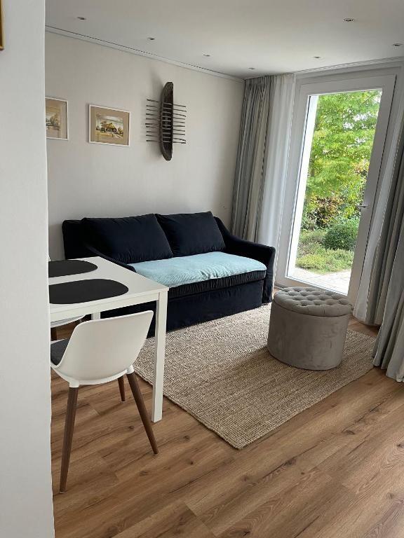 Wohnbereich mit Sofa, Tisch und Stuhl. Durchgang zur Terrasse mit Blick auf Garten.