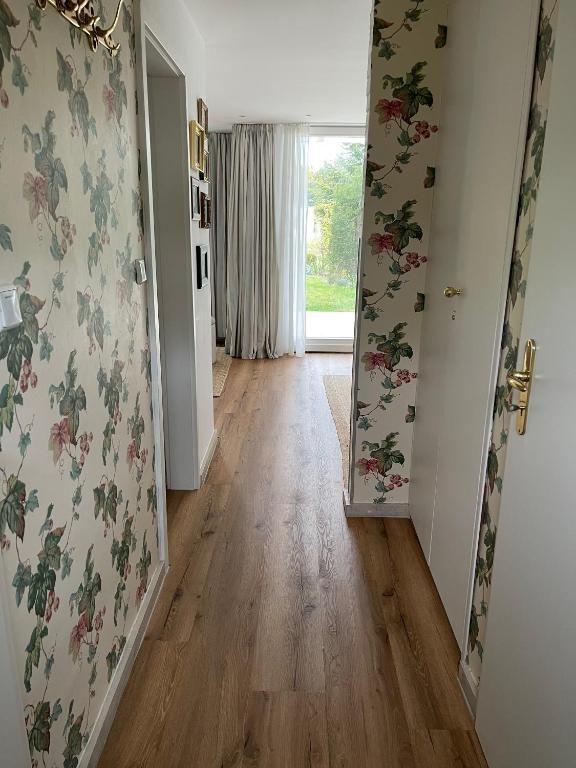 Flur mit Holzboden und floraler Tapete führt zu einem Fenster mit Blick nach draußen.