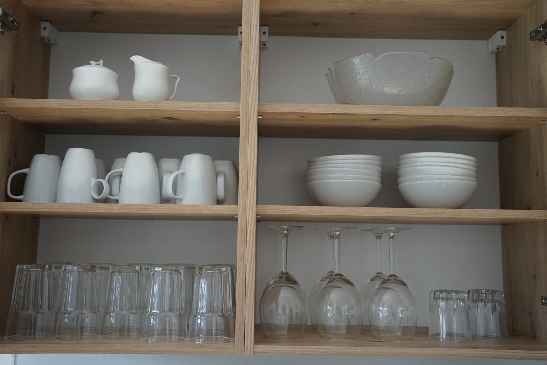 Wooden cabinet with dishes and glasses. White mugs, bowls, and wine glasses are visible.