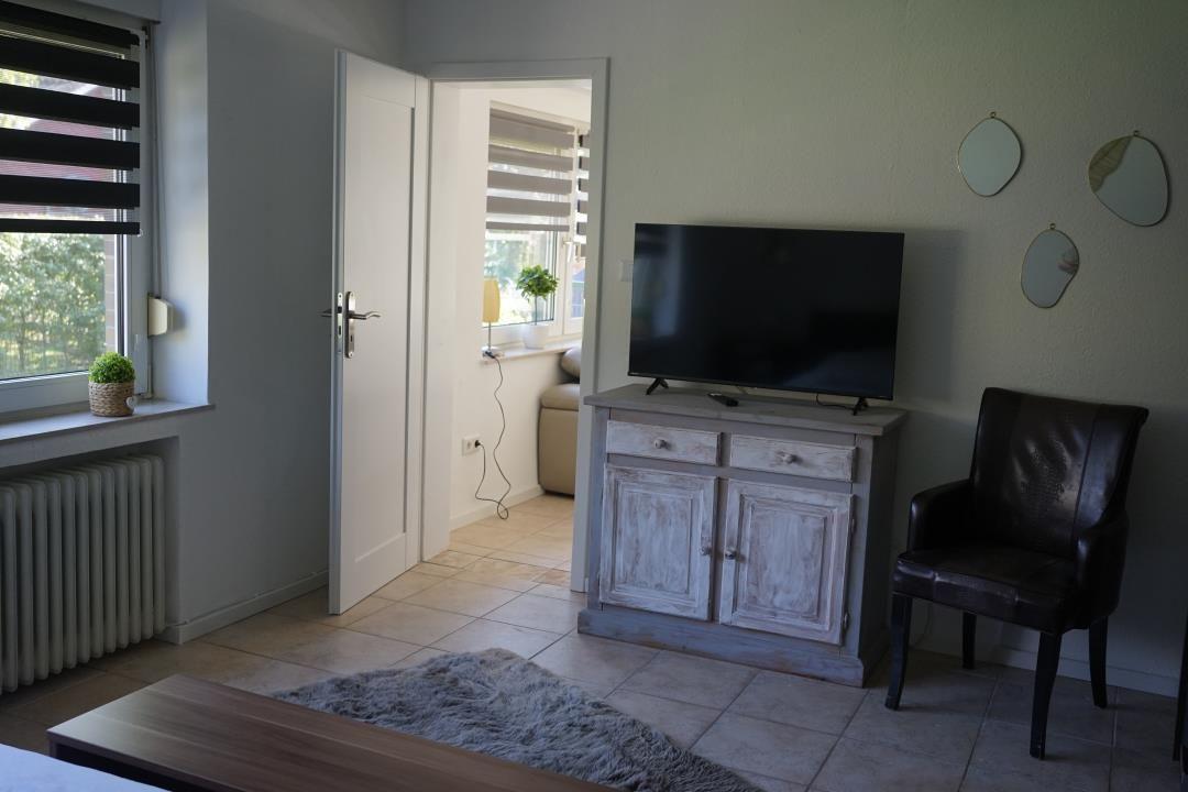 Living area with TV, leather chair, and window. Door leads to adjacent room.