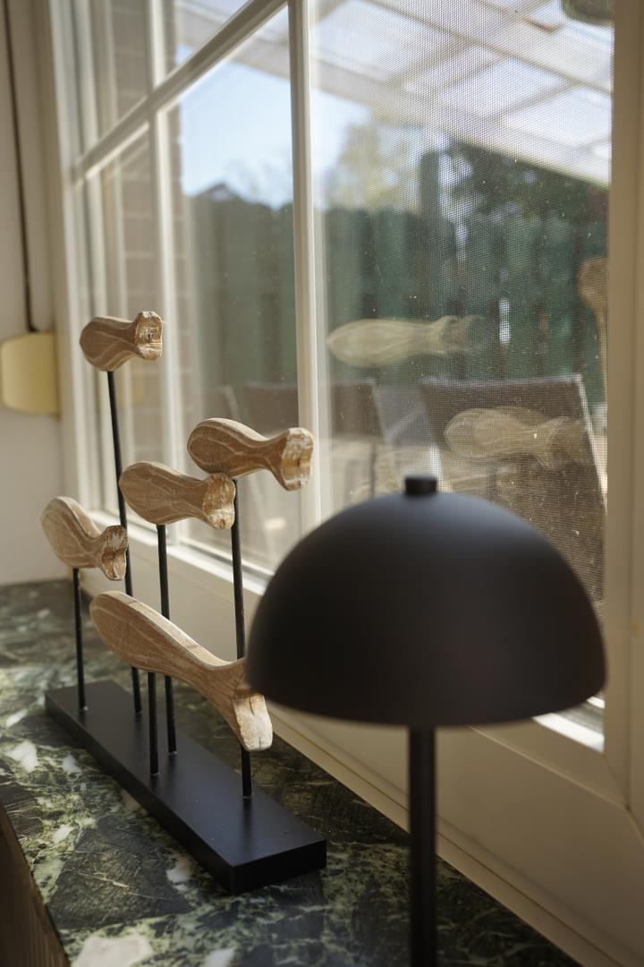 Wooden figures on a black stand sit on a marble countertop next to a window.