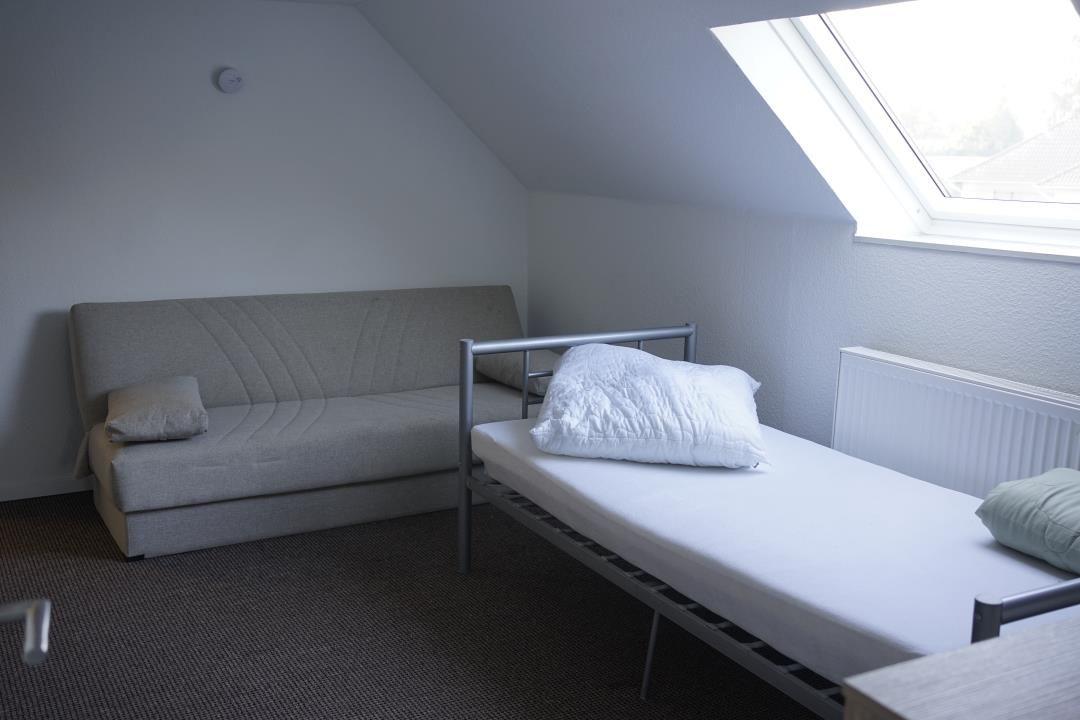 Room with sofa bed and single bed under sloped ceiling with skylight.