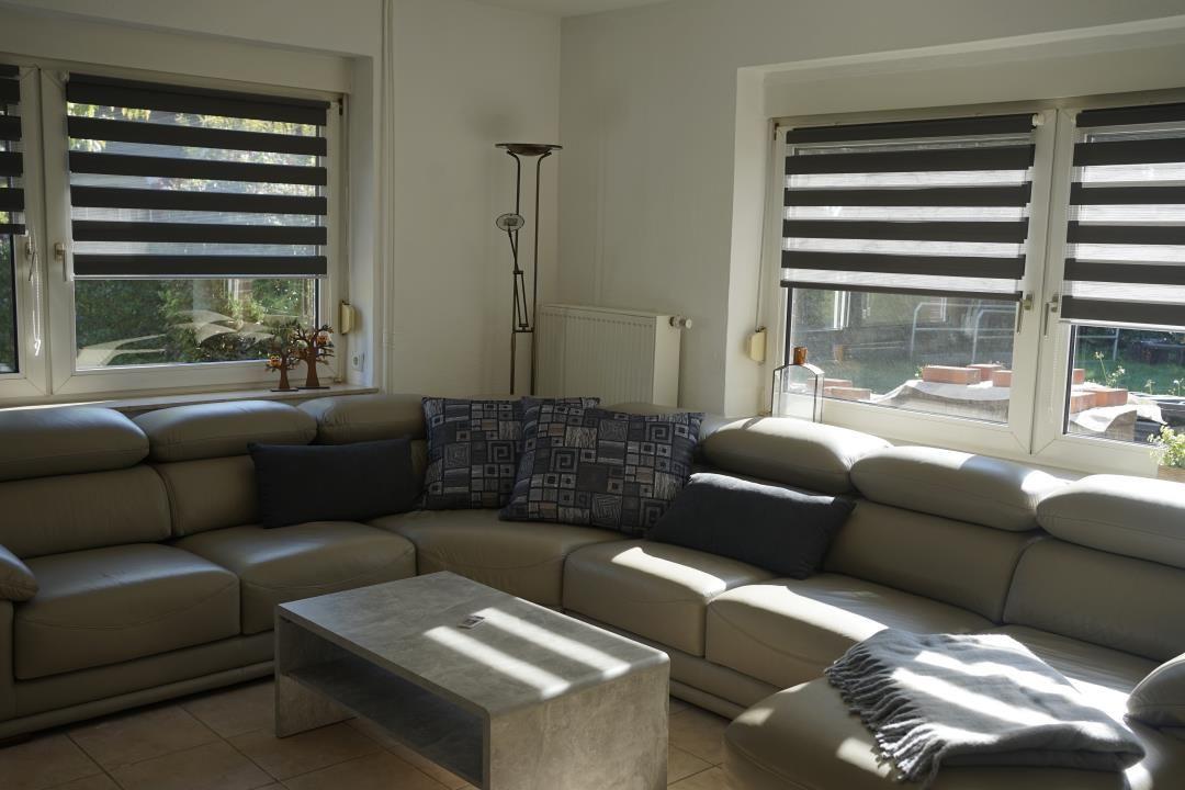 Living room with sectional sofa, coffee table, and windows with blinds.