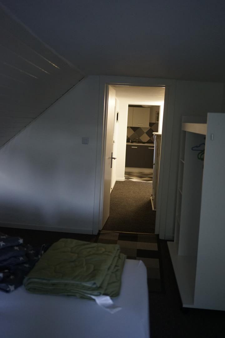 Bedroom with view into kitchen and closet. Sloped ceiling visible.