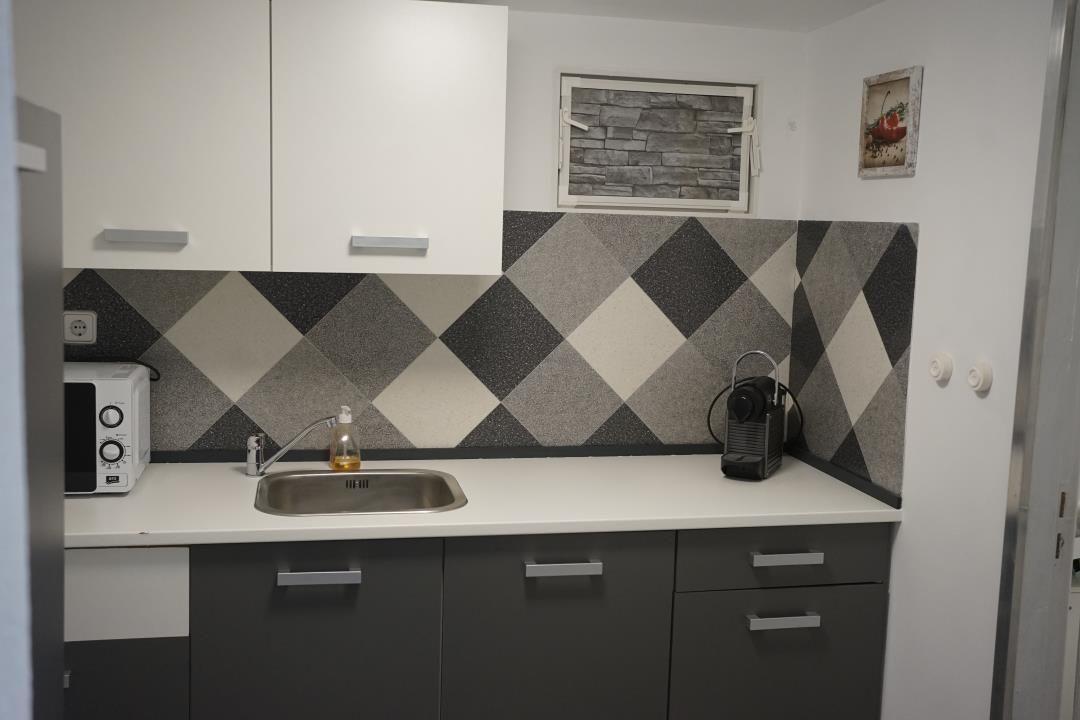 Kitchen with white surfaces, gray cabinets, and black-and-white mosaic on the wall.