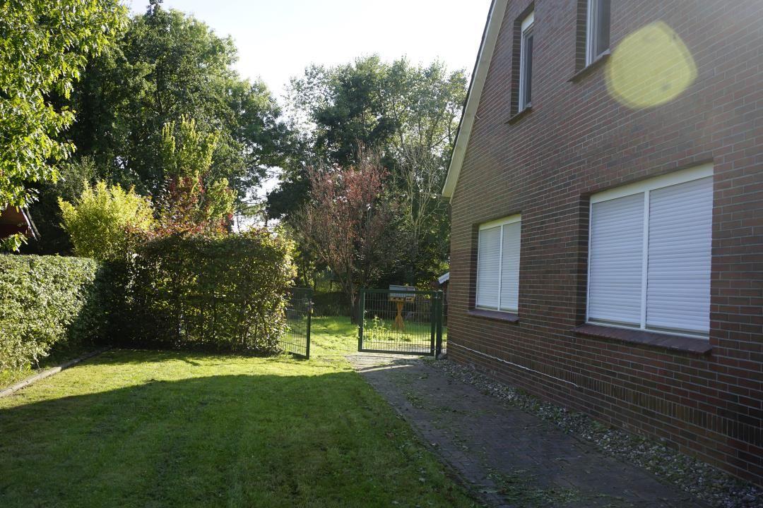 Backyard with lawn, hedge, and gate leading to a brick house with windows.